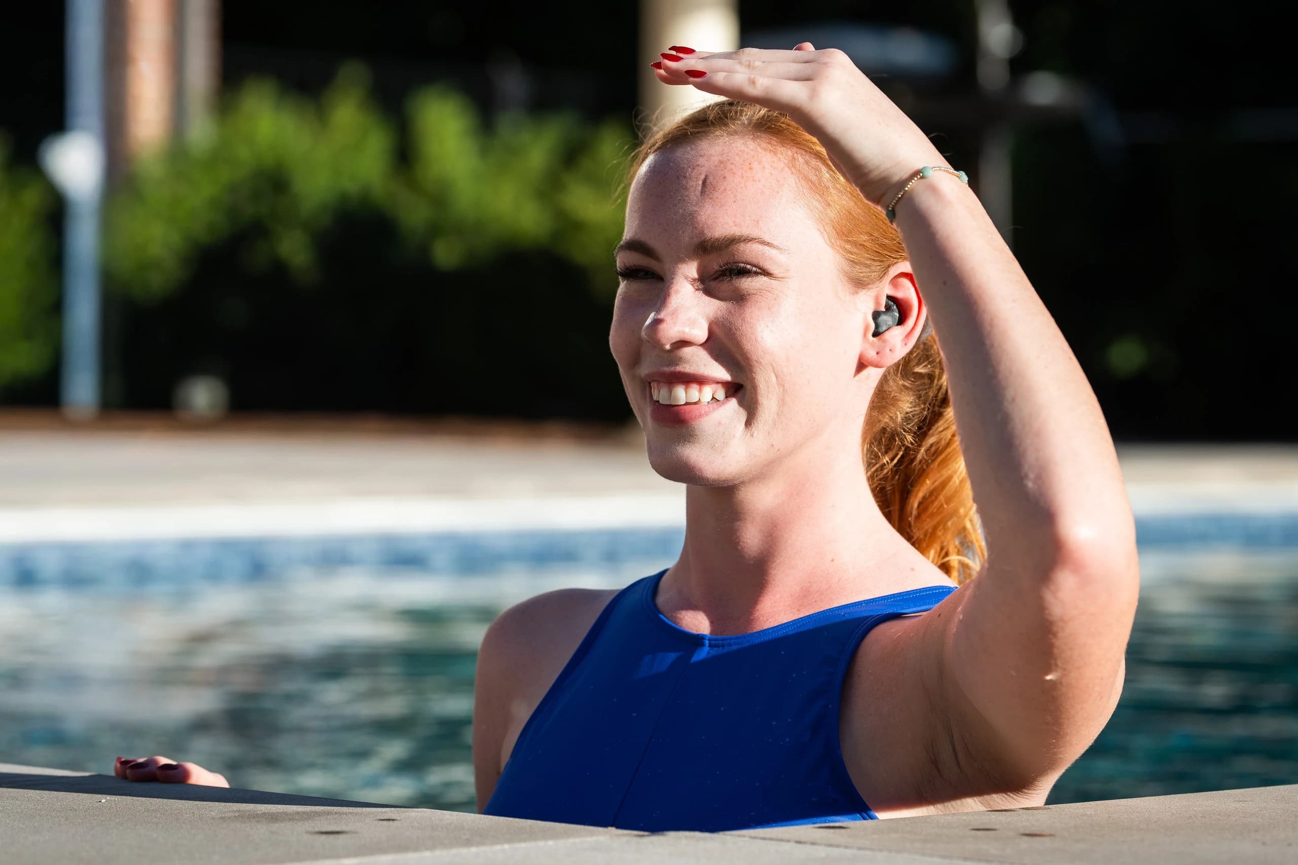 A swimmer at the wall, smiling, the bud in her ear